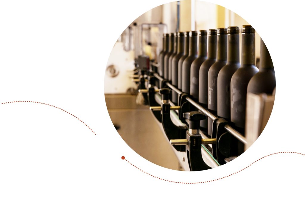 A production line in a bottling facility with a row of dark, wine bottles moving along a conveyor belt.